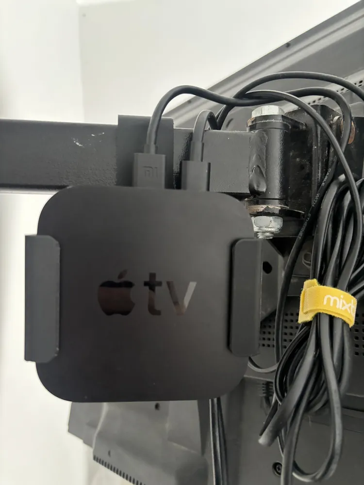 Black bracket holding an Apple TV box behind a screen